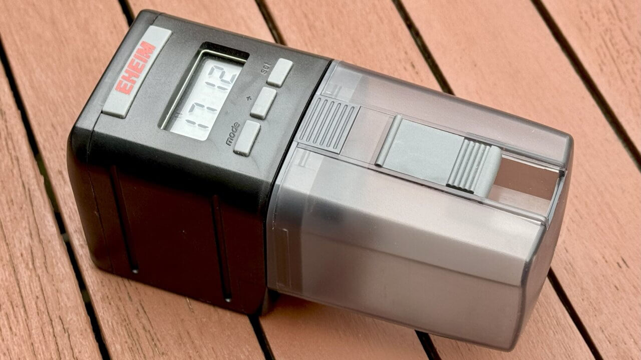 Eheim Futterautomat für Aquarien, auf einem Holztisch platziert. Die perfekte Fütterungslösung für ein Aquarium im Urlaub mit LCD-Anzeige und Futterkammer