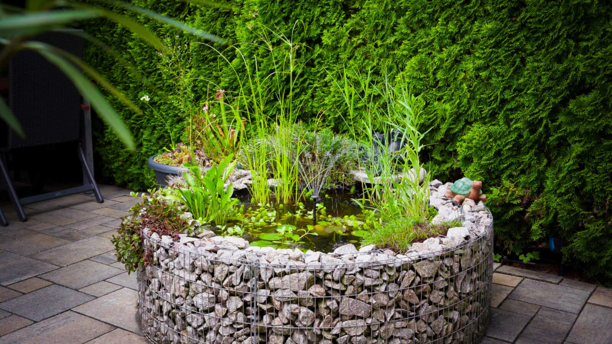 Bepflanzter Gabionen-Miniteich mit Seerose, Sumpfpflanzen und Solarfontäne auf einer Terrasse
